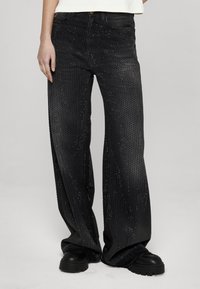 Fekete, széles szárú farmernadrág texturált felülettel, apró fém szegecsekkel díszítve az egész anyagon. Hagyományos, ötlovas zsebes kialakítású.