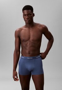 Boxer briefs Calvin Klein in tessuto blu scuro, con una cintura logo bianca. Il modello ha una fisicità tonica e si presenta con sicurezza.