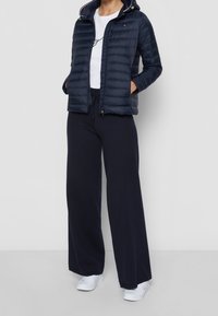 Marinblå pufferjacka med huva, ribbad krage och dragkedjefickor, tillsammans med löst sittande marinblå sweatpants och vita sneakers.