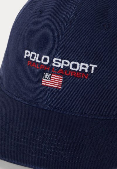 Σκούφος σε ναυτικό μπλε με κεντημένο το "POLO SPORT RALPH LAUREN" σε λευκό και κόκκινο πάνω από ένα μικρό ταμπελάκι με την αμερικανική σημαία.