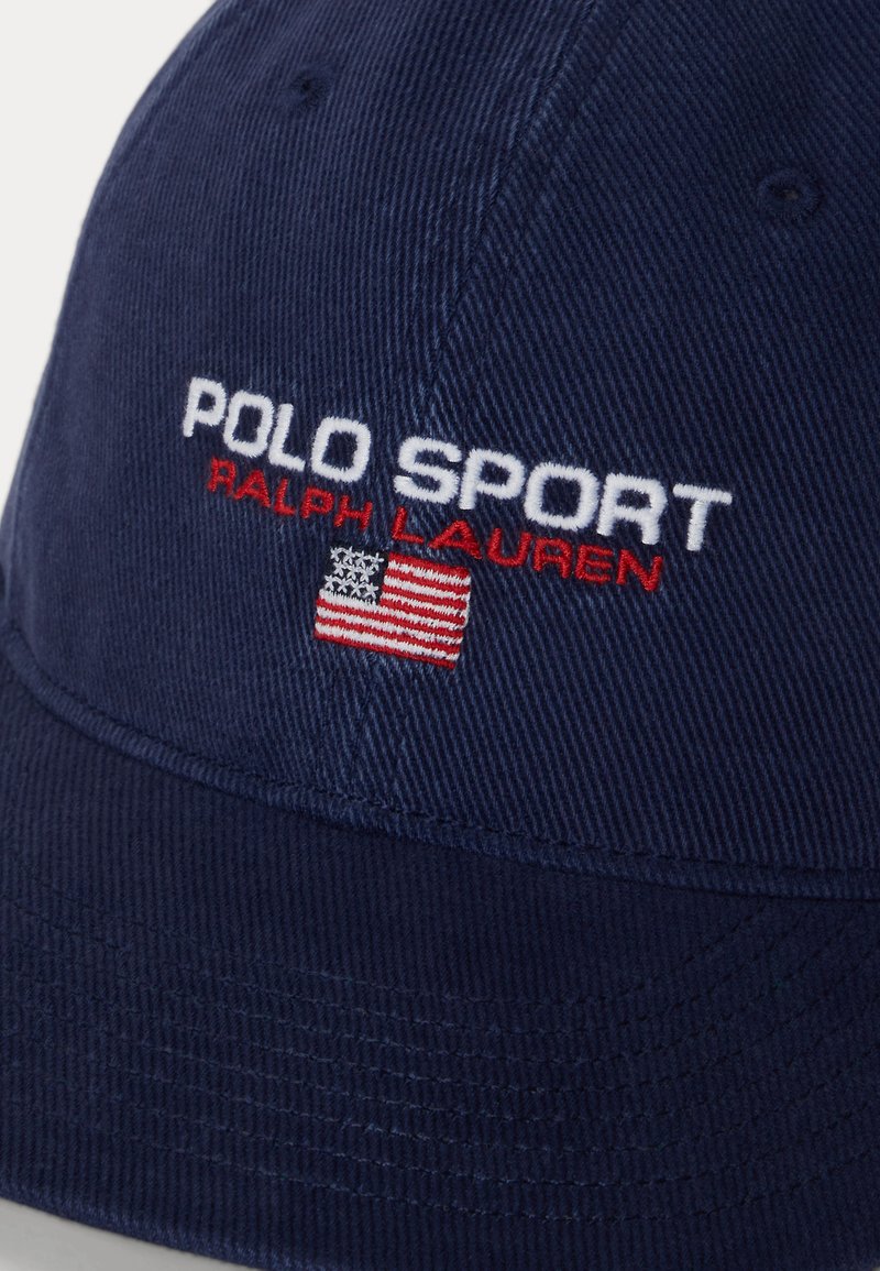 Gorra azul marino con "POLO SPORT RALPH LAUREN" bordado en blanco y rojo sobre un pequeño parche con la bandera estadounidense.