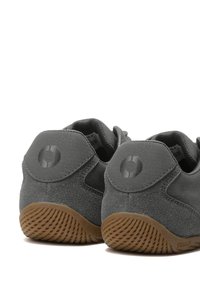 Paire de baskets en daim gris vues de dos avec des semelles marron texturées et un logo circulaire sur la languette du talon.