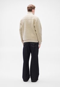 Bež flis jakna s visokim ovratnikom, tekstuiranim vanjskim dijelom i rebrastim manšetama, uparena s tamnim trapericama širokih nogavica.