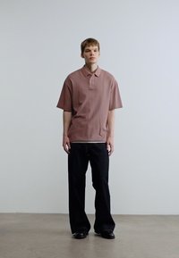 Κοντομάνικο, ριπ πουκάμισο πόλο σε απαλό ροζ, συνδυασμένο με φαρδιά μαύρη παντελόνια, με διπλωμένο γιακά και διακριτικές σχεδιαστικές λεπτομέρειες.