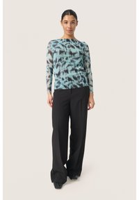Tricou cu maneci lungi imprimat, de culoare albastru deschis, cu modele abstracte negre; asortat cu pantaloni negri cu talie înaltă și picioare largi, împreună cu pantofi negri.