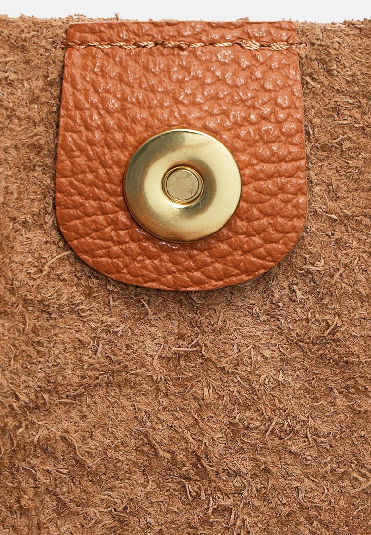 Braunes, raues Wildleder mit einem strukturierten, beige Lederlasche und einem runden, goldenen Magnetdruckknopf in der Mitte.