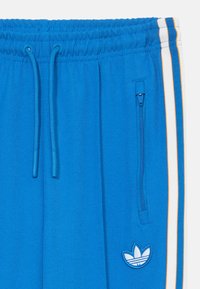 Blauwe sweatpants met een elastische tailleband met trekkoorden, zijzak met rits en witte en oranje strepen langs de benen. Inclusief logo-detail.