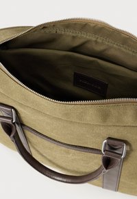 Olivengrøn lærreds taske med brune læderdetaljer og håndtag, med en lynlåslukning og en indvendig foret i en lignende mørkegrøn farve.