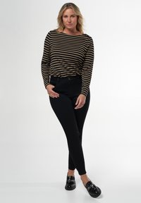 Top à manches longues rayé en noir et beige, pantalon noir ajusté et chaussures noires avec détail en chaîne, sur fond blanc.