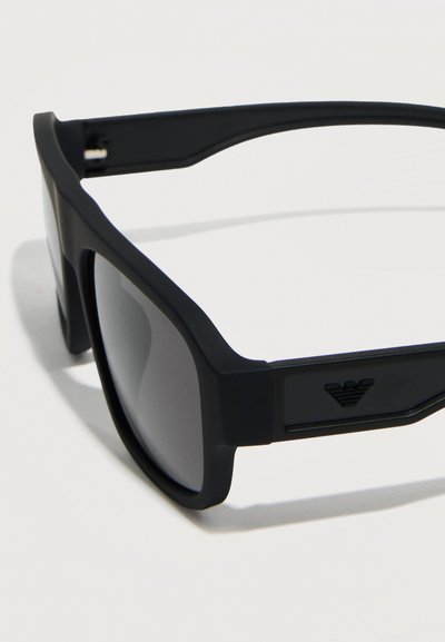 Μαύρα ορθογώνια γυαλιά ηλίου με ματ σκελετό και σκουρόχρωμους φακούς, με ένα μικρό ανάγλυφο λογότυπο στο πλαϊνό σκέλος.