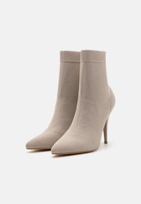 Bottines chaussettes beiges à bout pointu, tige côtelée et talon haut fin ; confectionnées dans un matériau en maille extensible pour un effet ajusté.