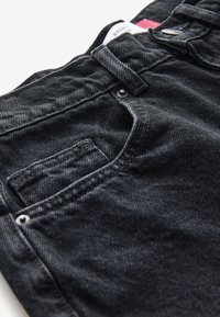Schwarze Jeans aus Denim mit strukturiertem Stoff, ausgestattet mit einer Vordertasche, Knopfverschluss und Gürtelschlaufen. Etikett am Bund sichtbar.