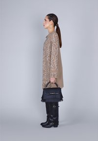 Abito beige a maniche lunghe con ricami in perline a motivo paisley, abbinato a stivali neri sopra il ginocchio e una borsa nera con frange dotata di manico.