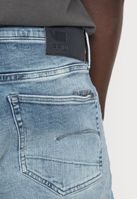 Ljusblå jeans i denim har en bakficka med subtil söm och en svart läderlapp. Texturen är mjuk med en urblekt finish.