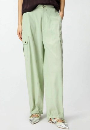 Pantaloni verde chiaro a gamba larga con bottoni frontali e tasche a patta, indossati con ballerine argento a punta e top scuro.