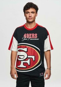 Sort og rød oversized T-shirt med teksten "49ERS San Francisco" og det store "SF" logo i midten. Fremstillet af bomuldsmateriale med kontrastærmer.