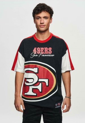 T-shirt surdimensionné noir et rouge avec le texte "49ERS San Francisco" et un grand logo "SF" au centre. Matière en coton avec des manches contrastées.