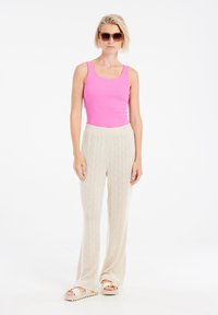 Roze geribbelde tanktop gecombineerd met beige gewatteerde wijde broek; model draagt een paarse zonnebril en beige sandalen met accenten.
