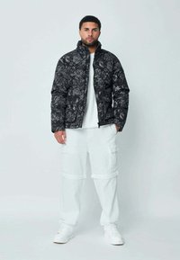 Doudoune florale noire avec un col montant, fermeture éclair et deux poches avant, associée à un pantalon cargo blanc et des baskets blanches.