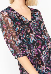 Svart klänning med ett färgglatt paisley-mönster, i ett strukturerat tyg och V-ringad design; korta ärmar med uppvikta manschetter.