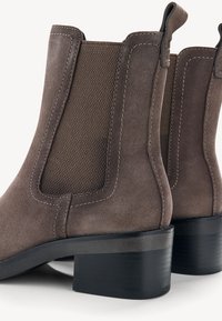 Bottines en daim marron avec panneaux élastiques sur les côtés, talon noir épais et coutures décoratives sur les côtés.