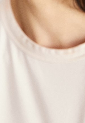 Close-up of a person's collarbone and neck wearing a light beige round-neck shirt.