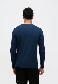 Μπλούζα με μακριά μανίκια σε σκούρο μπλε χρώμα, κατασκευασμένη από μαλακό ύφασμα με στρογγυλή λαιμόκοψη, χαρακτηρίζεται από λεία υφή και απλό σχέδιο, φαίνεται από το πίσω μέρος.