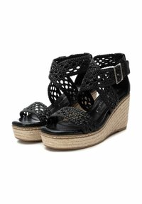 Sandalias de cuña tejidas en negro con un upper de tela texturizada y una plataforma de yute trenzado. Presentan una correa en el tobillo con un hebilla de tono plateado y un diseño de punta abierta.