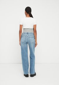 Top ceñido gris claro y blanco con mangas cortas, combinado con unos jeans de tiro alto, holgados, de color azul claro y unos zapatos negros gruesos.