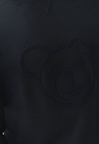 Sudadera de color azul oscuro con un diseño de oso bordado y suave en el pecho. La tela tiene una textura lisa con un cuello acanalado.