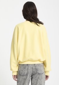 Zachte, gele fleece sweatshirt met een casual pasvorm, geribbelde manchetten en onderrand. Gepaard met grijze denim jeans. De textuur lijkt pluizig en gezellig.