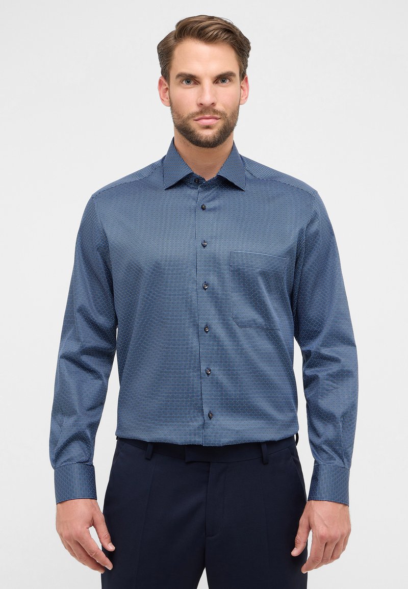 Camicia a maniche lunghe di colore blu navy con motivo geometrico. Collare e taschino frontale. Bottoni marroni per la chiusura.