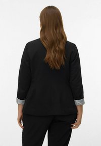 Zwarte blazer met een getailleerde pasvorm, voorzien van driekwartmouwen en een omgeslagen manchet met een zilverkleurige gestreepte voering. Gladde textuur, minimale details.