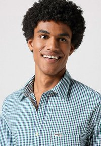 Koszula zapinana na guziki w kratkę w zielonym, niebieskim i białym kolorze, wykonana z bawełny. Posiada kołnierzyk, kieszonkę oraz subtelne logo z boku.