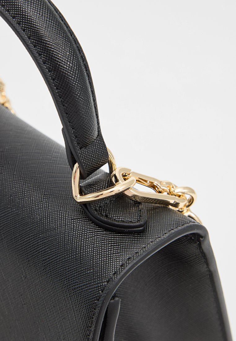 Primo piano di una tracolla di una borsa in pelle nera con texture, attaccata con un moschettone in metallo dorato e hardware rettangolare su un corpo in pelle nera liscia.