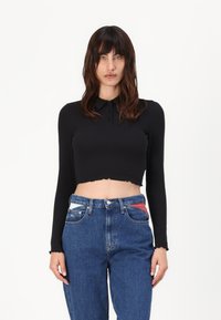 Svart avkortet langermet skjorte med krage og knappdetaljer, parret med blå høyt midje jeans med fargerike lommeakcenter.