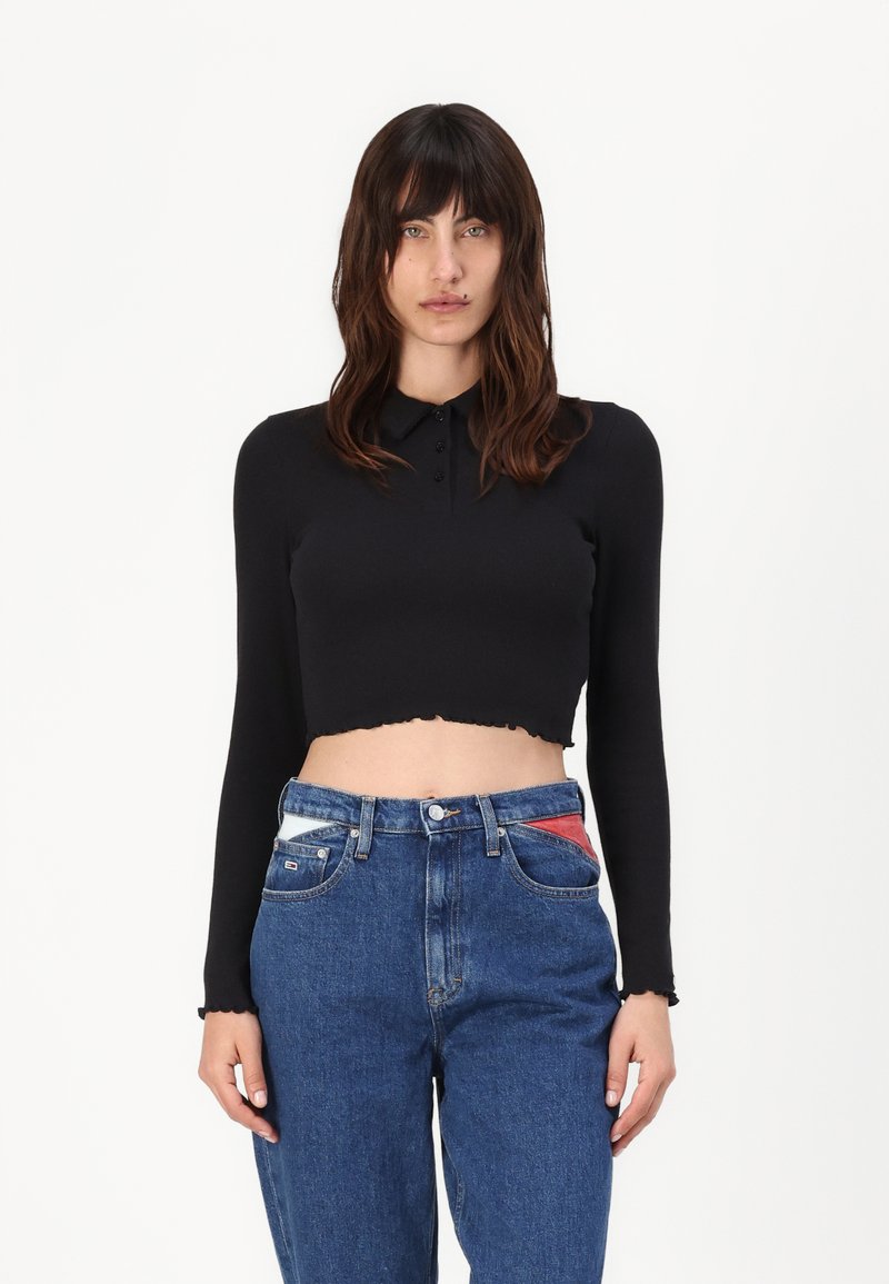 Svart avkortet langermet skjorte med krage og knappdetaljer, parret med blå høyt midje jeans med fargerike lommeakcenter.