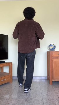 Casaco de veludo cotelê castanho com um ajuste descontraído, combinado com jeans pretos largos e ténis pretos. Superfície suave, design sem adornos.