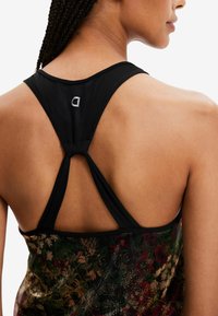 Mustan urheilullinen tank top, jossa on ristiselkämalli. Kukallinen kuvio vihreänä, punaiseen ja kultaisena; logotieto kaulassa.