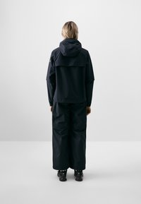 Black waterproof jacket with a hood, featuring a loose fit and large pockets. The fabric appears smooth and matte, suitable for outdoor activities.