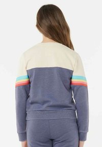 Felpa di colore blu navy con uno yoke beige, presenta strisce multicolori sulle maniche. Il materiale è morbido, con una vestibilità comoda e polsini a coste.