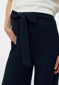 Marineblaue, hochtaillierte Hose aus strukturiertem Stoff mit einem gebundenen Schleifenakzent an der Taille und weitem, lässigem Bein.