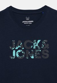 Temno modra bombažna majica z okroglim izrezom. Spredaj je velik napis "JACK & JONES" v črni in svetlo modri barvi s pikčastim vzorcem.