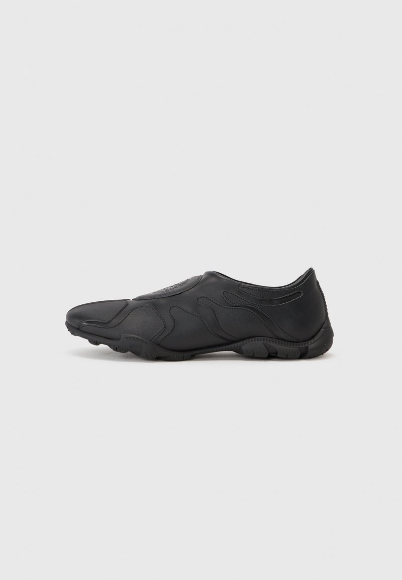 Zapato negro con un diseño elegante, textura suave y acentos de superficie ondulados. Punta redonda y suela de goma con un perfil bajo.