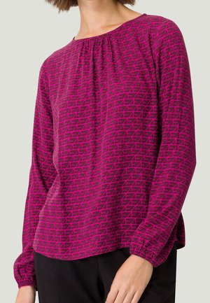 Blouse à manches longues en magenta vif avec un motif géométrique. Dispose d'un col rond et de poignets froncés pour un ajustement décontracté.