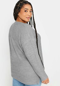 Grå stickad tröja med en texturerad yta, med långa ärmar och sidossprund. Matchas med ljusblå jeans.