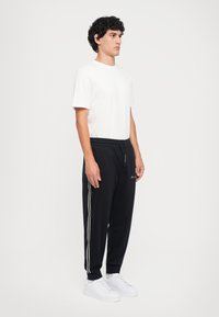 Sorte joggebukser med hvite sidepaneler og elastisk midje, kombinert med en hvit t-skjorte med rund hals og hvite sneakers.