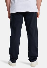 Donkerblauwe katoenen broek met een relaxte pasvorm, zichtbare stiksels en elastische boorden, gecombineerd met witte sneakers.