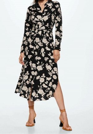 Femme portant une robe midi noire à manches longues avec un imprimé floral beige et des sandales à talons hauts couleur camel avec bride à la cheville, debout jambes écartées.