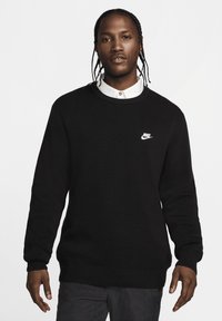 Μαύρη πλεκτή μπλούζα με στρογγυλή λαιμόκοψη και μακρύ μανίκι. Διαθέτει το λευκό λογότυπο Nike στην αριστερή πλευρά του στήθους και ριμπ μανίκια και στρίφωμα.